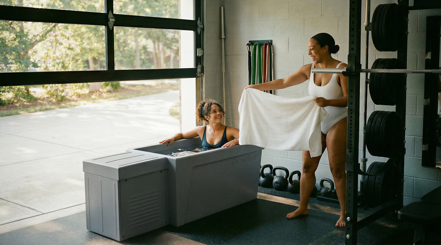 Two women in a home gym setting with exercise equipment and a bathtub.