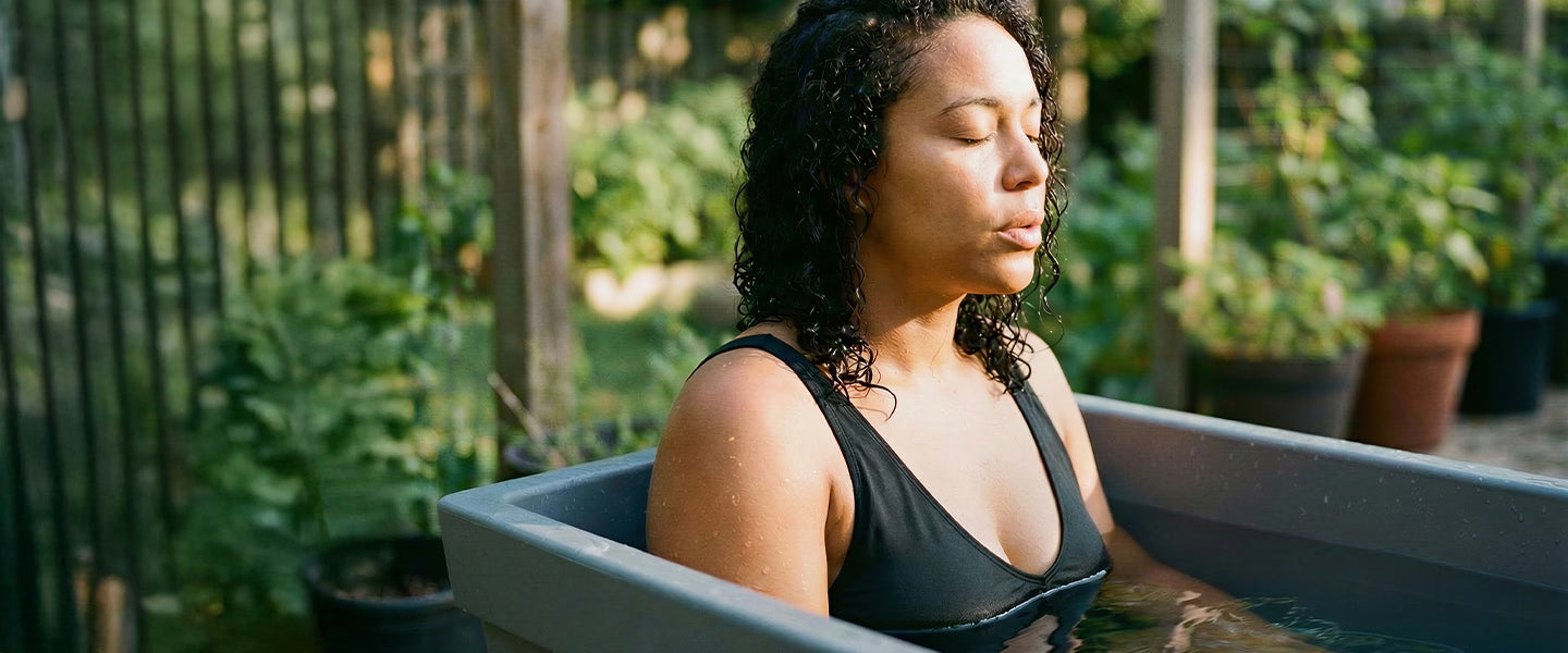 Woman meditating sitting in a cold plunge bath surrounded by greenery